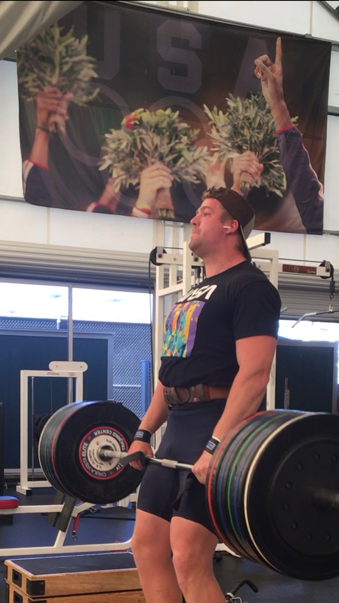 Mike lifting a loaded barbell under a Team USA banner